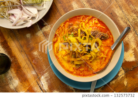 Traditional Thai noodle soup served with fresh garnishes on a rustic wooden table 132573732