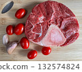 Top-down view of raw beef shank steak with bone, arranged with fresh cherry tomatoes and garlic cloves on a wooden board. Ideal for food blogs, recipe illustrations and cooking stock photography. 132574824