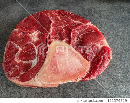 Side view of a raw beef shank steak with visible bone, placed on a dark stone countertop. High-resolution image with juicy texture, perfect for recipes, food blogs, packaging and culinary stock. 132574829
