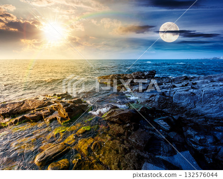 beautiful view of rocky sea coast under dramatic sky. day and night time change concept. scenic summer solstice landscape of beach under sun and moon at twilight. coastal background with large stones beautiful view of rocky sea coast under dramatic sky. day and night time change concept. scenic summer solstice landscape of beach under sun and moon at twilight. coastal background with large stones 132576044
