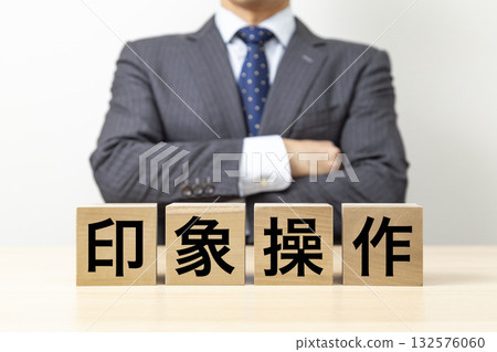 A businessman with his arms crossed and a block with the word "impression manipulation" written on it A businessman with his arms crossed and a block with the word "impression manipulation" written on it 132576060