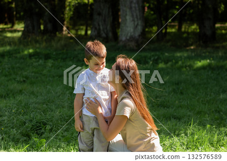 Young Caucasian mother laughs giggling son across sunny park lawn. Dynamic image radiates pure joy, energy, and fun of outdoor playtime together. Young Caucasian mother laughs giggling son across sunny park lawn. Dynamic image radiates pure joy, energy, and fun of outdoor playtime together. 132576589