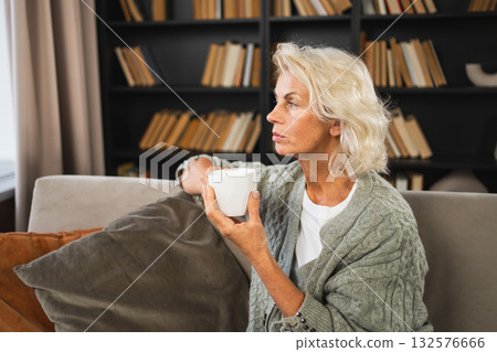 Good morning autumn winter fall vibe. Comfort relaxed senior old elderly woman drinking hot beverage tea coffee in sofa at home. Mature woman resting enjoy calm morning at home alone. Pension concept 132576666