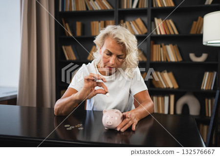 Saving money investment for future. Senior adult mature woman putting money coin in piggy bank. Old grandmother counting saving money planning retirement budget. Investment banking concept Saving money investment for future. Senior adult mature woman putting money coin in piggy bank. Old grandmother counting saving money planning retirement budget. Investment banking concept 132576667