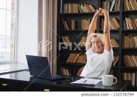 Middle aged senior woman relaxing stretching arms and body taking break from work on laptop at home. Older mature woman happy after work done satisfied by good result. Fatigue from long laptop usage Middle aged senior woman relaxing stretching arms and body taking break from work on laptop at home. Older mature woman happy after work done satisfied by good result. Fatigue from long laptop usage 132576794