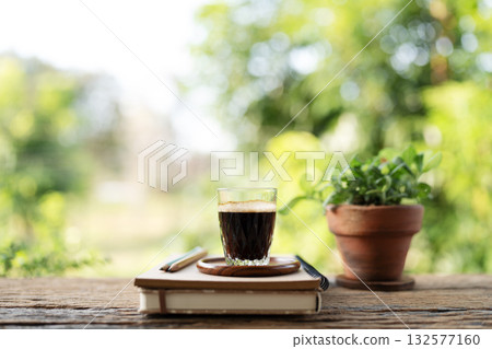Americano coffee glass cup and old book on rustic wooden table with potted plant Americano coffee glass cup and old book on rustic wooden table with potted plant 132577160
