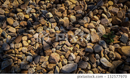 texture of a natural assortment of pebbles and river stones in warm earth tones, ideal for landscaping, garden borders, pathways, or decorative rock surfaces 132577970
