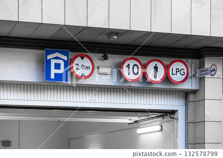 Underground parking garage entrance with regulatory signs for height, speed, and LPG vehicle restrictions, emphasizing driver safety and car traffic awareness 132578799