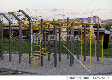 Outdoor calisthenics park featuring diverse yellow and gray fitness equipment, including rings and a punching bag, fostering street workout and urban health Outdoor calisthenics park featuring diverse yellow and gray fitness equipment, including rings and a punching bag, fostering street workout and urban health 132578803