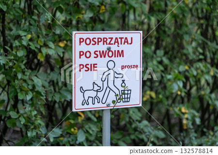 A public sign encouraging dog owners to clean up after their pets, promoting urban cleanliness and responsible pet ownership in a park setting 132578814