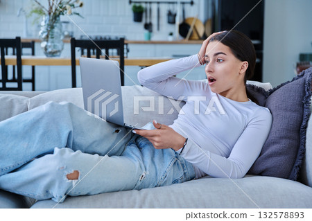 Surprised teenage girl looking at laptop, lying on sofa at home Surprised teenage girl looking at laptop, lying on sofa at home 132578893