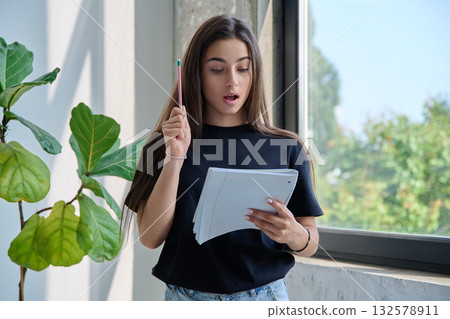 Portrait of teenage college student girl with notebook pencil at home near window 132578911