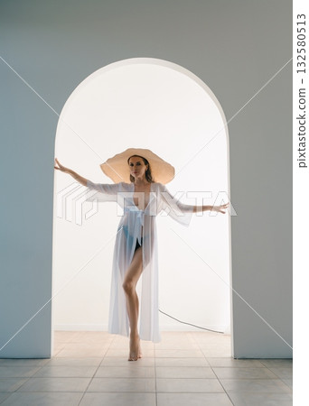 Woman Wearing a White Dress and Large Hat Posing in an Archway Woman Wearing a White Dress and Large Hat Posing in an Archway 132580513