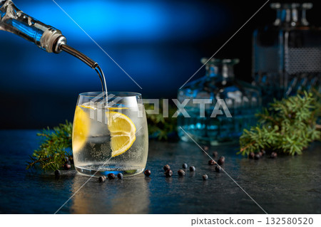 Gin is poured from a bottle into a glass with ice and lemon slice. 132580520