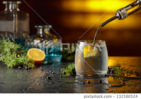 Gin is poured from a bottle into a glass with ice and lemon slice. 132580524