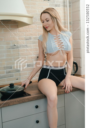 Blonde Woman Cooking In Kitchen Wearing Blue Top And Black Shorts Blonde Woman Cooking In Kitchen Wearing Blue Top And Black Shorts 132580552