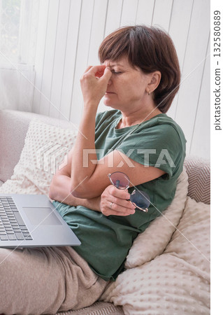 Caucasian mature female experiencing eye strain while using laptop at home. 132580889