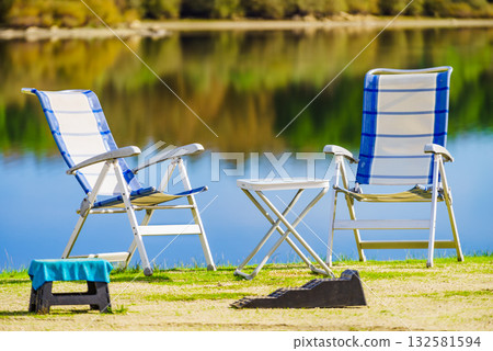 Two empty camp chairs on lake shore Two empty camp chairs on lake shore 132581594