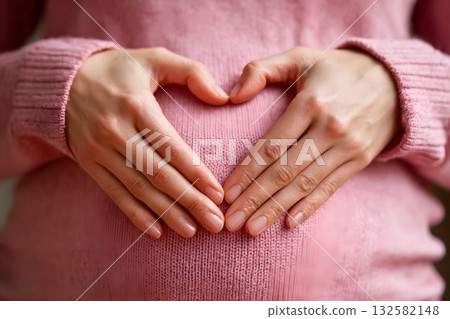 Pregnant belly with hands forming a heart shape over it. 132582148