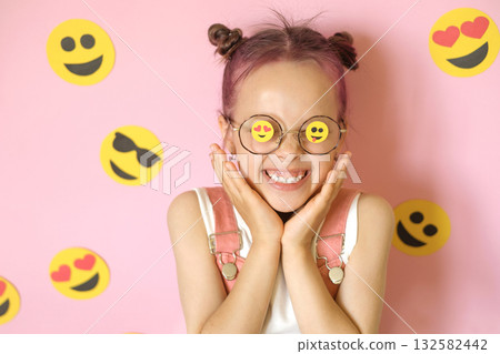 A laughing, cheerful girl with glasses and a variety of emoji icons. 132582442