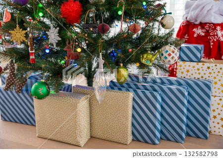 Wrapped gifts under decorated Christmas tree with glowing ornaments and festive lights at home 132582798