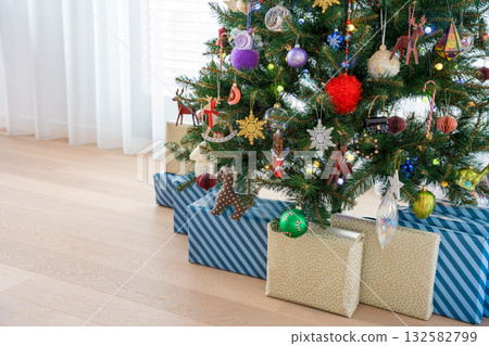 Wrapped gifts under decorated Christmas tree with glowing ornaments and festive lights at home. 132582799