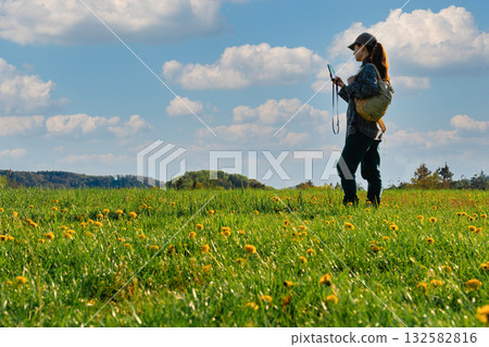 Woman using smartphone for navigation in spring meadow with blooming dandelions in Czech countryside Woman using smartphone for navigation in spring meadow with blooming dandelions in Czech countryside 132582816