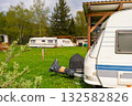 Retro caravans and camper trailers parked on spring meadow campsite with wooden shelters and trees 132582826