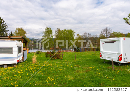 Two retro camper trailers parked on green grass near lake with wooden shelter, copy space Two retro camper trailers parked on green grass near lake with wooden shelter, copy space 132582827