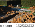 Close-up view of a construction site trench filled with gravel and surrounded by piles of soil. 132582832