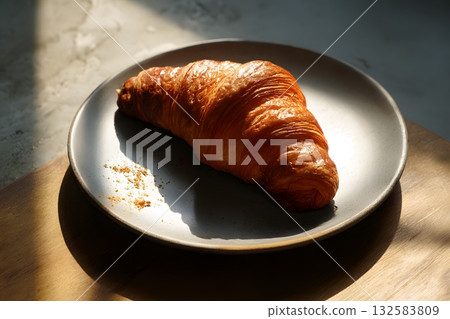 A golden croissant rests on a plate in the soft morning light. 132583809