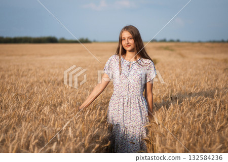 Beautiful girl in light dress in the field of ripe grain. Beautiful photo of a cheerful blond girl in agricultural field 132584236