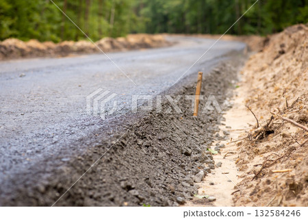 Close-up photo of new asphalt road pavement in the countryside. Constructing new high-quality road in the woods Close-up photo of new asphalt road pavement in the countryside. Constructing new high-quality road in the woods 132584246