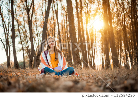 Cheerful girl having pleasant time in autumn park, reading books, enjoying the beauty of nature. Melancholic autumn atmosphere in the park 132584250