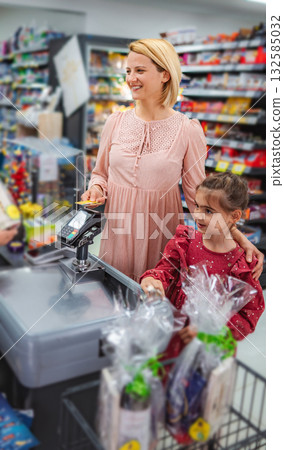 Mother and daughter using contactless payment at grocery checkout Mother and daughter using contactless payment at grocery checkout 132585032