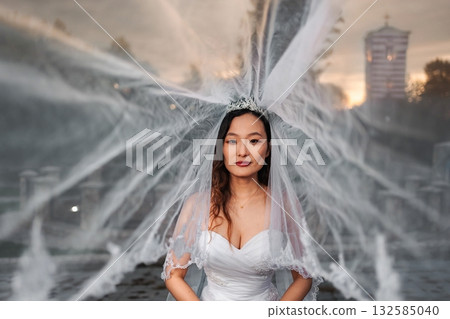 Chinese bride wearing wedding dress and veil by fountain Chinese bride wearing wedding dress and veil by fountain 132585040