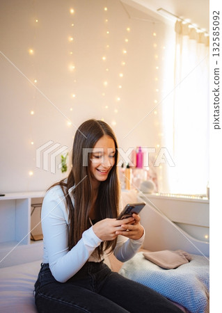 Teenager girl smiling texting on phone in bedroom Teenager girl smiling texting on phone in bedroom 132585092
