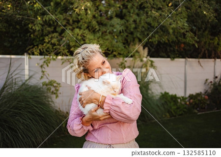 Adult woman holding and hugging a white fluffy cat in a garden Adult woman holding and hugging a white fluffy cat in a garden 132585110