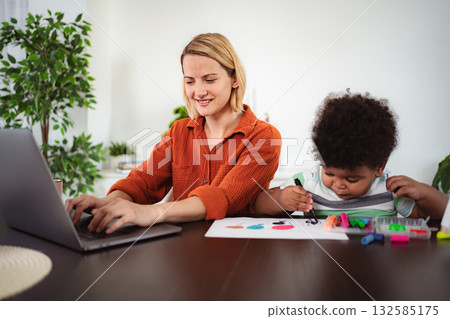 Mother working remotely while child drawing at home Mother working remotely while child drawing at home 132585175