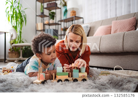 Mother and son playing with wooden toy train on living room floor Mother and son playing with wooden toy train on living room floor 132585176