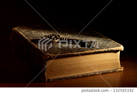 A photo of an antique key resting on an ornate antique book 132585192