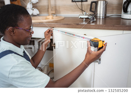 Carpenter taking measurements of kitchen cabinet using tape measure 132585200