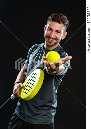 Smiling man holding yellow ball and paddle ready for paddle tennis game indoors 132585354