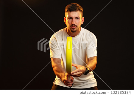 Man practicing with a yellow training tool in a dark setting during a sports session Man practicing with a yellow training tool in a dark setting during a sports session 132585384
