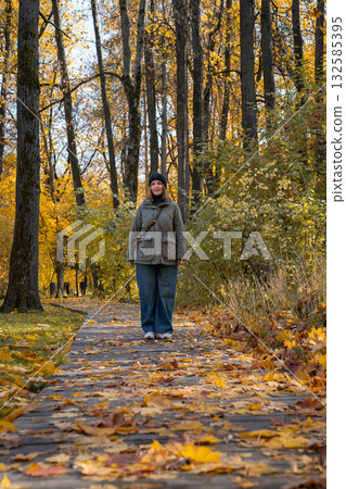 Woman walks through an autumn park in warm sunlight, wearing a khaki jacket and jeans surrounded by yellow leaves Woman walks through an autumn park in warm sunlight, wearing a khaki jacket and jeans surrounded by yellow leaves 132585395
