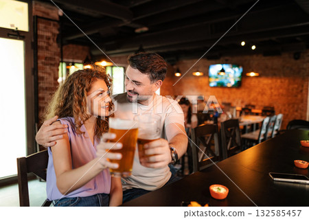 Couple drinking beer and eating snacks at the counter in a pub Couple drinking beer and eating snacks at the counter in a pub 132585457