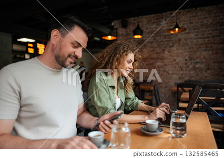 Young Couple Working on Devices and Drinking Coffee in Cafe Young Couple Working on Devices and Drinking Coffee in Cafe 132585465