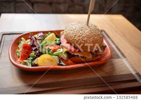 Delicious gourmet burger with fresh salad served in a cozy cafe setting Delicious gourmet burger with fresh salad served in a cozy cafe setting 132585488