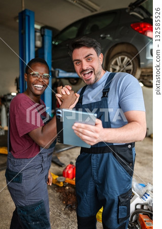 Mechanics shaking hands and holding a tablet in a garage Mechanics shaking hands and holding a tablet in a garage 132585526