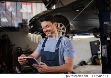 Mechanic Smiling and Using Digital Tablet in Auto Repair Shop Mechanic Smiling and Using Digital Tablet in Auto Repair Shop 132585531